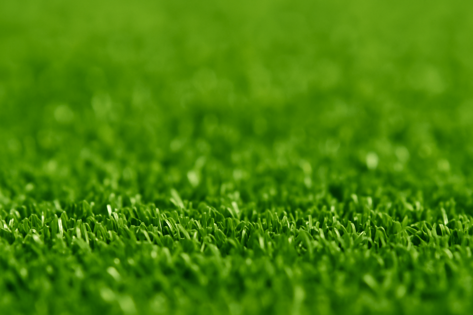 Macro close-up of premium artificial turf for golf flooring, showing individual shock-absorbing golf surface fibers in sharp focus against a softly blurred background.